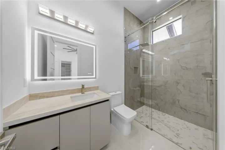 Bathroom with vanity, tile walls, and illuminated mirror with integrated defogging feature.