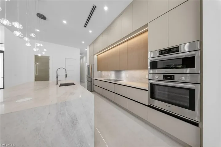 Dual tone kitchen featuring stainless steel appliances, modern cabinets, pendant lighting, light quarts countertops, and a kitchen island with sink.