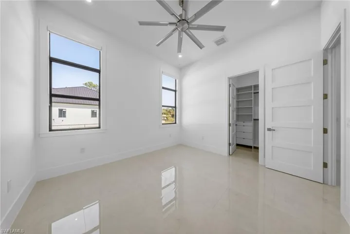 Bedroom featuring a walk-in closet, ensuite bathroom, oversize windows for natural light, curtains, and a ceiling fan.