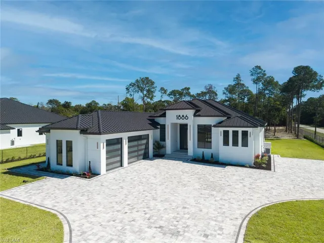 Front of house with metal roof, glass paneled garage doors, oversized windows/door, and paver driveway.