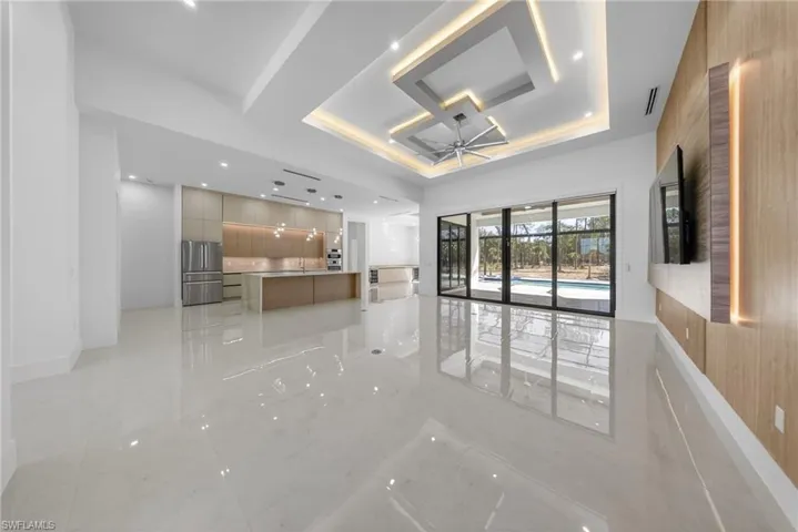 Living room with a 14' 4" tray ceiling, custom kitchen, 10ft sliding doors with curtains, modern TV wall, recessed lighting, ceiling fan, and open floor plan.