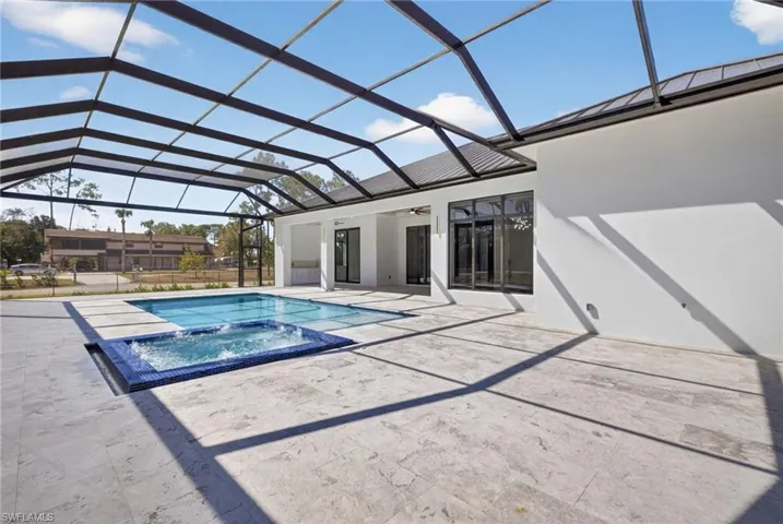 Combined pool / hot tub withing a screen enclosure. A patio area with summer kitchen. Marble decking throughout.