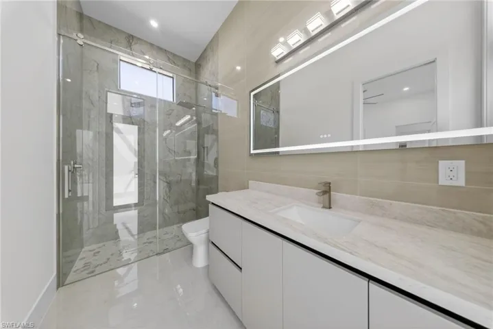 Bathroom with vanity, tile walls, and illuminated mirror with integrated defogging feature.