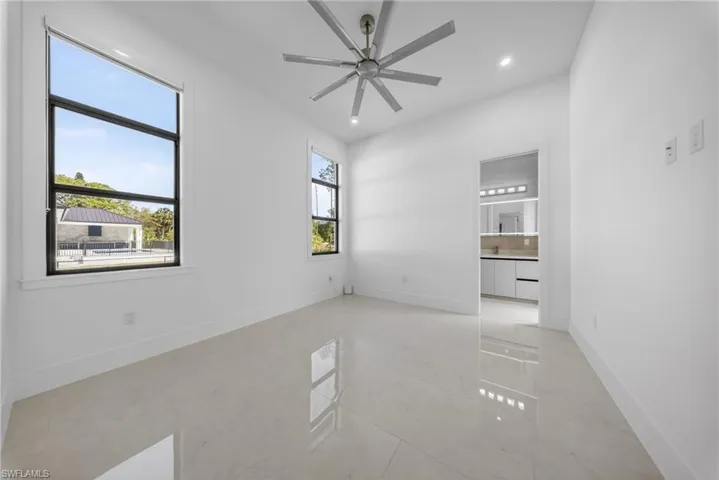 Bedroom with pool access featuring a walk-in closet, ensuite bathroom, oversize windows for natural light, curtains, and a ceiling fan.