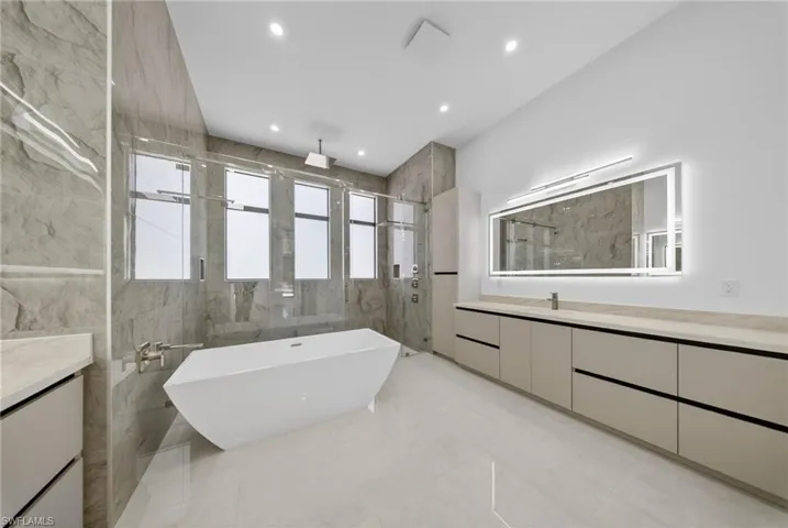 Master bathroom with vanity, a freestanding tub, a marble finish shower, recessed lighting, and tile walls.