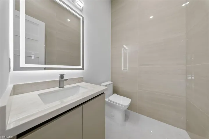 Bathroom with vanity, tile walls, and illuminated mirror with an integrated defogging feature.