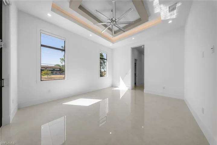 Master bedroom with ceiling fan, recessed lighting, a tray ceiling, and oversized windows with curtains. Sliding doors for convenient pool deck access.