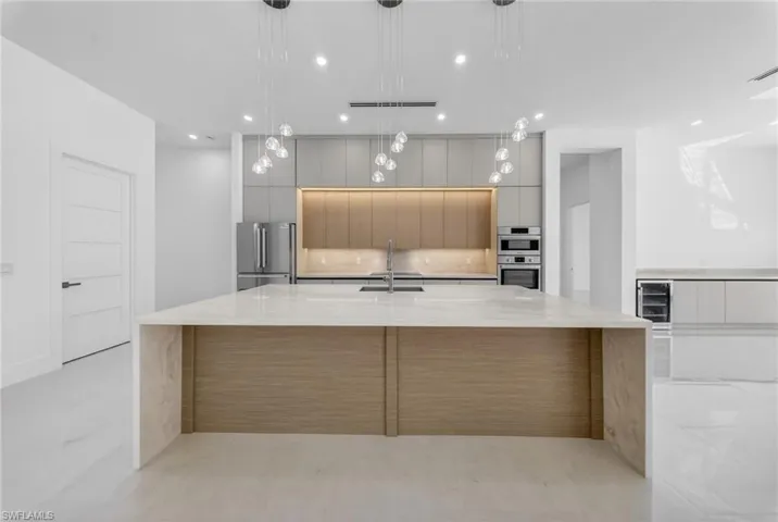 Kitchen featuring modern custom cabinets, quartz countertops, stainless steel appliances, a large island with sink, and hanging light fixtures.