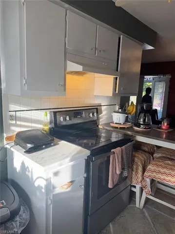 Kitchen with stainless steel electric range, light countertops, tasteful backsplash, and gray cabinetry