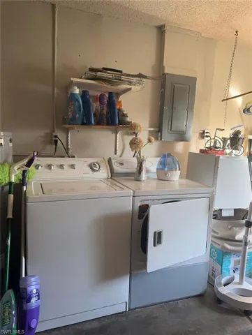 Laundry area with electric panel, concrete floors, washing machine and clothes dryer, and a textured ceiling