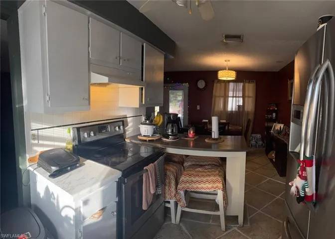 Kitchen featuring black range with electric stovetop, stainless steel fridge, decorative backsplash, dark tile patterned flooring, and light countertops