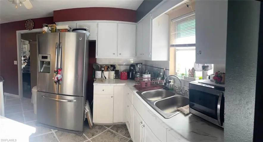 Kitchen featuring stainless steel appliances, white cabinetry, light countertops, light tile patterned floors, and backsplash