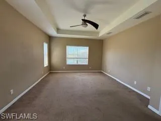Carpeted empty room with ceiling fan, a raised ceiling, baseboards, and visible vents