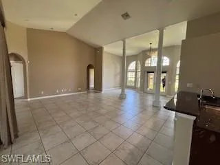 Unfurnished living room with decorative columns, visible vents, lofted ceiling, arched walkways, and light tile patterned flooring