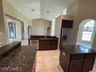 Kitchen featuring dark stone countertops, appliances with stainless steel finishes, arched walkways, and lofted ceiling