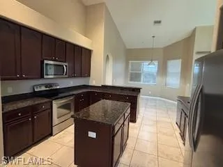Kitchen with dark stone countertops, appliances with stainless steel finishes, light tile patterned floors, and dark brown cabinetry