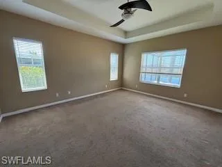 Carpeted empty room with a raised ceiling, baseboards, and a ceiling fan