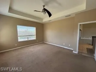 Empty room featuring carpet flooring, baseboards, a raised ceiling, and ceiling fan