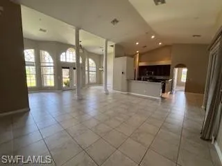 Unfurnished living room featuring lofted ceiling, arched walkways, baseboards, and light tile patterned floors