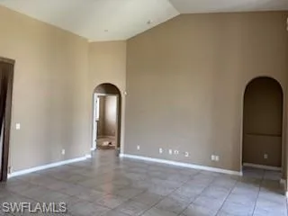 Unfurnished room featuring arched walkways, baseboards, and vaulted ceiling
