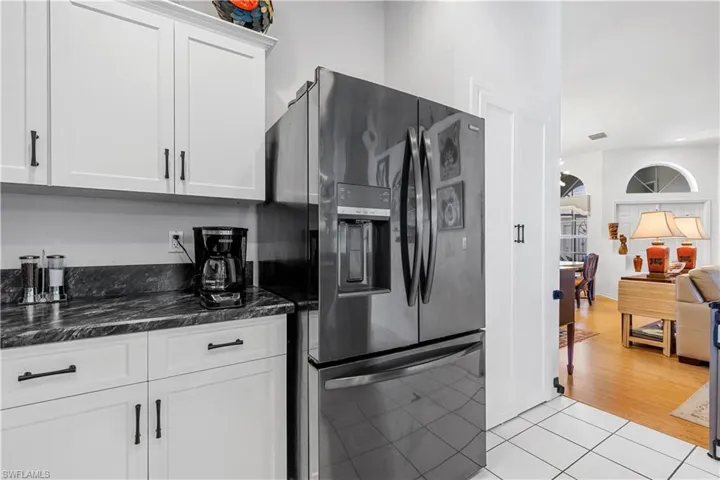 Kitchen with light tile patterned flooring, white cabinetry, dark stone countertops, and fridge with ice dispenser