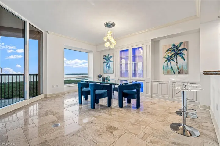 Dining space featuring crown molding, a chandelier, light marble finish floors, and a water view
