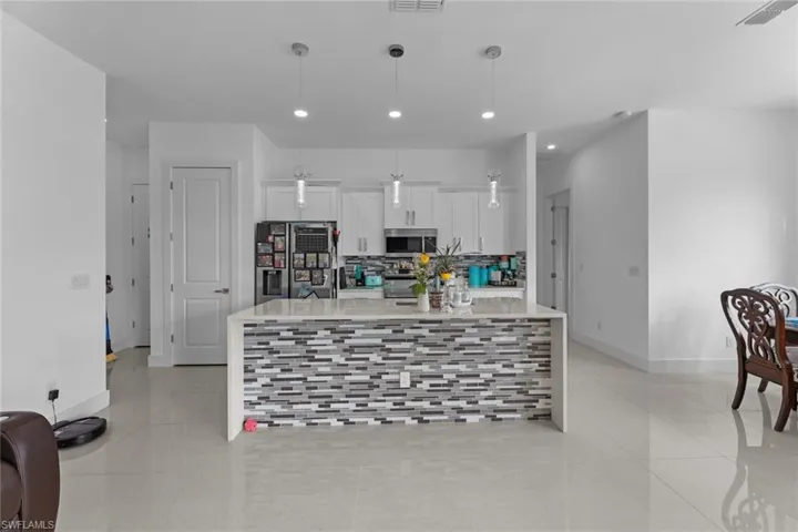 Kitchen featuring a kitchen island, appliances with stainless steel finishes, white cabinets, decorative light fixtures, and light tile flooring