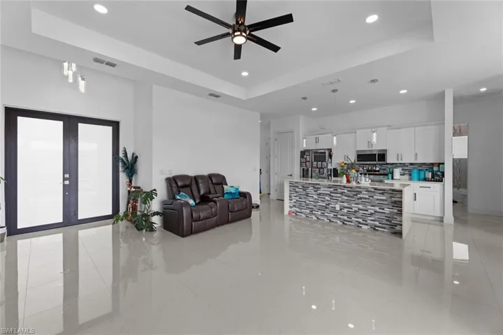 Living room featuring ceiling fan, a raised ceiling, french doors, and light tile floors