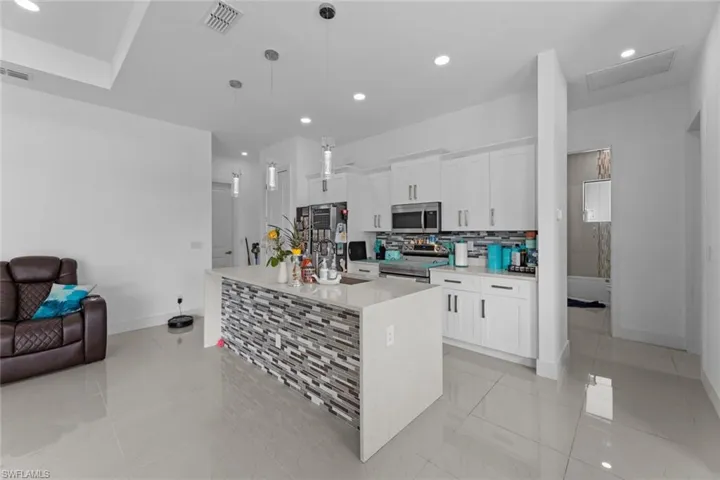 Kitchen with an island with sink, light tile floors, decorative light fixtures, and appliances with stainless steel finishes