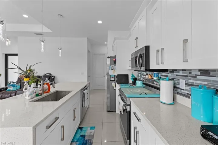 Kitchen with appliances with stainless steel finishes, white cabinets, light stone counters, sink, and tasteful backsplash