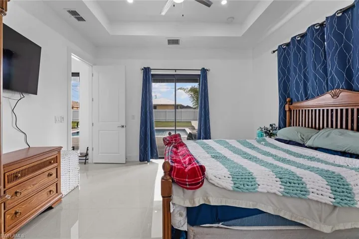 Tiled bedroom featuring ceiling fan, a tray ceiling, and access to exterior