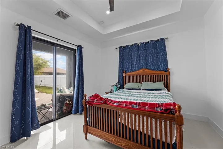Bedroom with ceiling fan, light tile flooring, a tray ceiling, and access to outside