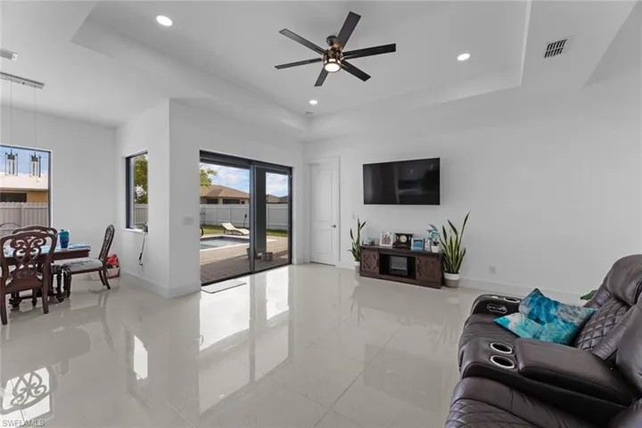 Living room with ceiling fan, a tray ceiling, and light tile floors