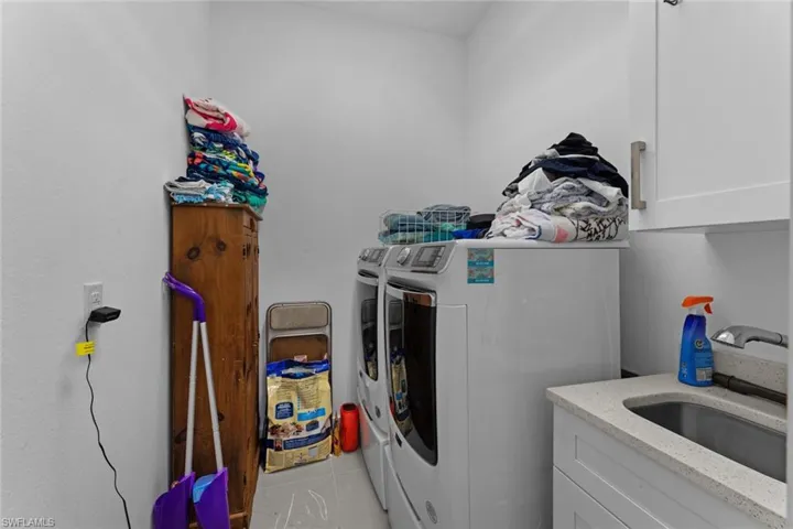 Clothes washing area with washing machine and dryer, sink, cabinets, and light tile floors