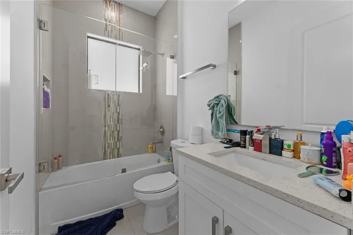 Full bathroom with tiled shower / bath, oversized vanity, tile flooring, and toilet