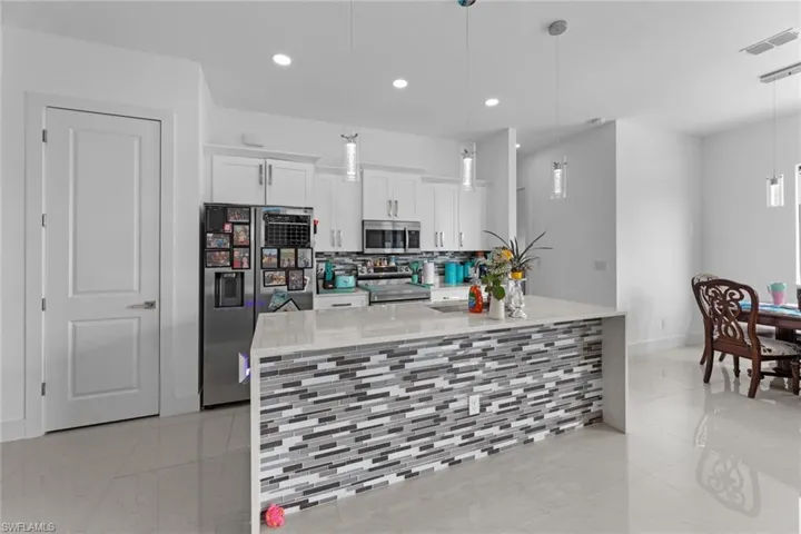 Kitchen featuring appliances with stainless steel finishes, hanging light fixtures, backsplash, and light tile floors
