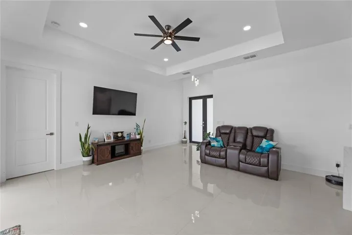Tiled living room featuring ceiling fan, a raised ceiling, and french doors