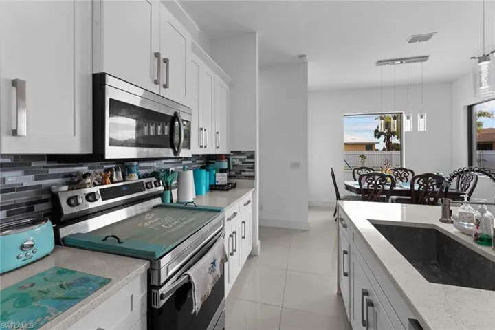 Kitchen with decorative light fixtures, backsplash, sink, white cabinets, and appliances with stainless steel finishes