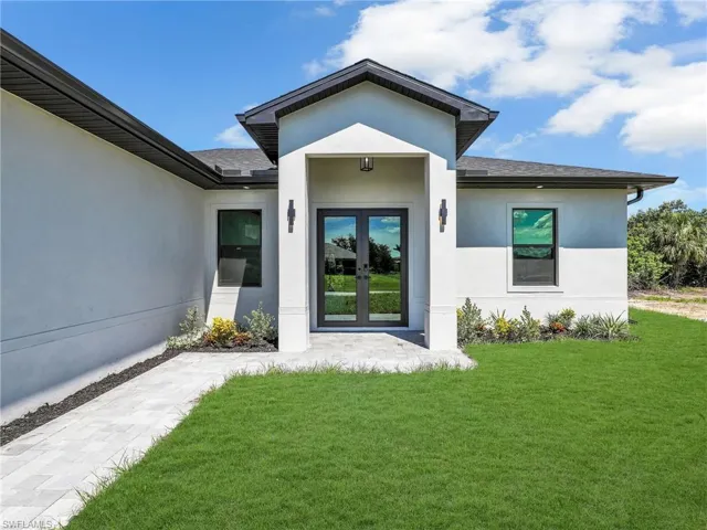 View of exterior entry featuring stucco siding, a yard, french doors, and roof with shingles