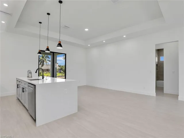 Kitchen with a tray ceiling, light stone countertops, decorative light fixtures, light wood-type flooring, and recessed lighting
