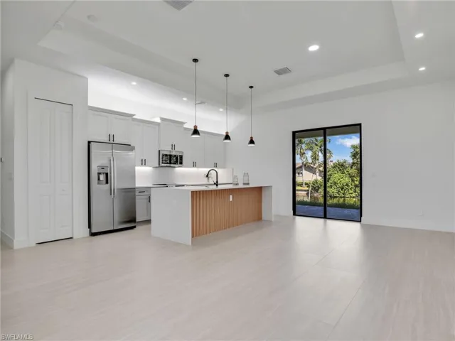 Kitchen with a raised ceiling, open floor plan, decorative light fixtures, stainless steel appliances, and white cabinets