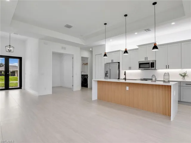 Kitchen featuring pendant lighting, a spacious island, appliances with stainless steel finishes, a raised ceiling, and recessed lighting