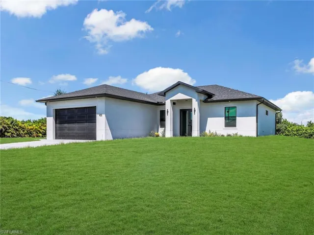View of front of property featuring a front lawn, stucco siding, a garage, and driveway