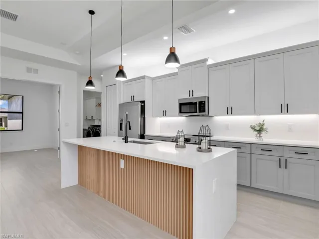 Kitchen with separate washer and dryer, pendant lighting, stainless steel appliances, a center island with sink, and light stone counters