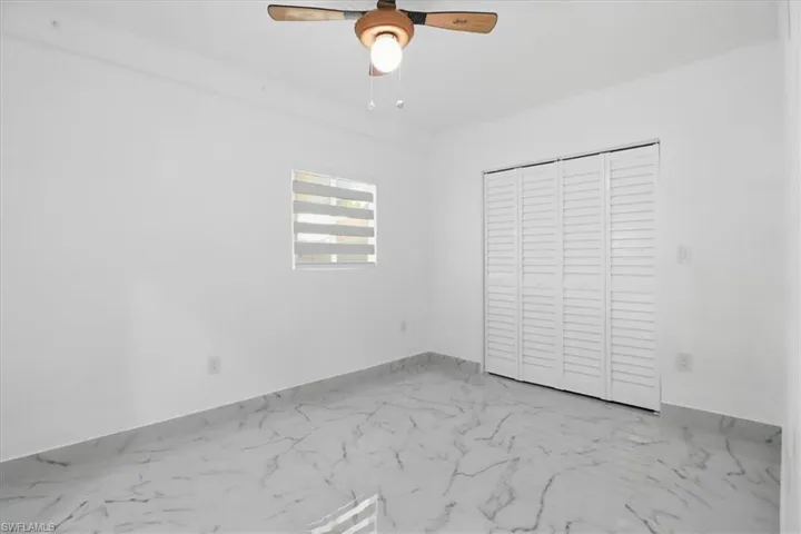 Unfurnished bedroom with marble look tiles, a closet, and a ceiling fan