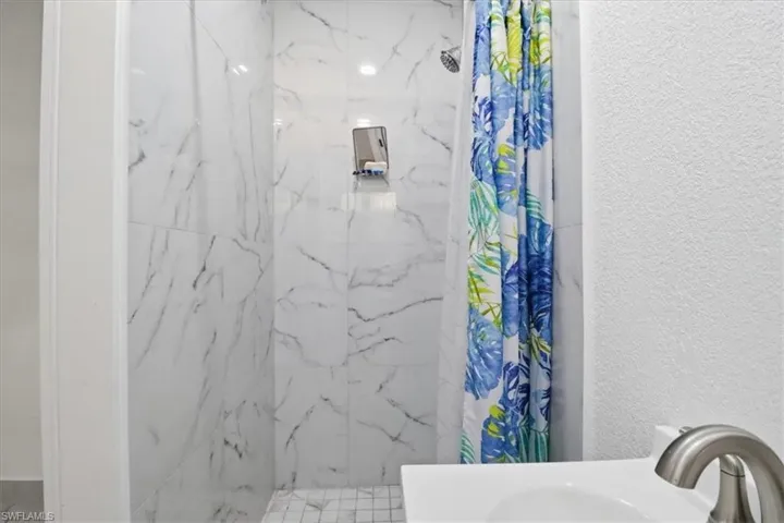 Full bathroom with a marble finish shower, a textured wall, and vanity