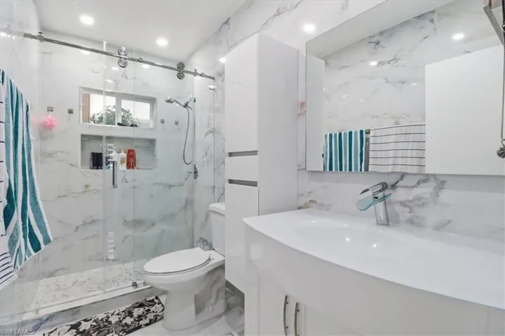 Full bath featuring vanity, a marble finish shower, stone wall, tile walls, and recessed lighting