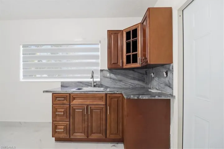 Bar area featuring brown cabinets, decorative backsplash, glass insert cabinets, and dark stone countertops
