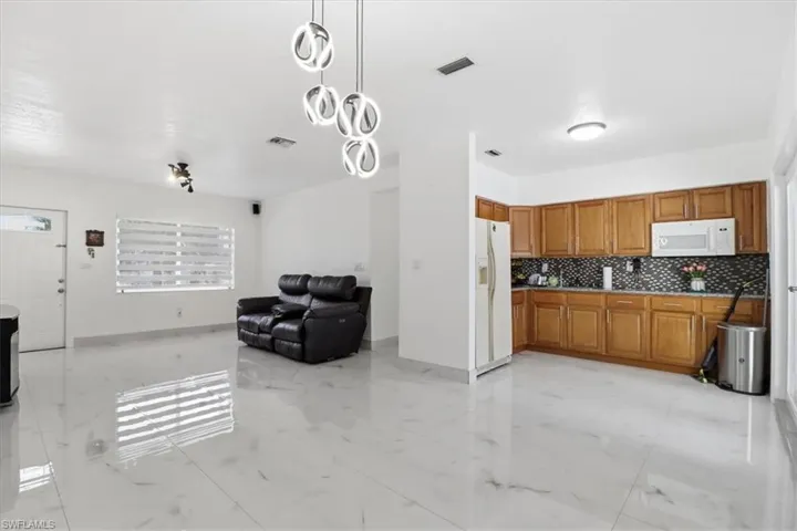 Kitchen featuring brown cabinetry, open floor plan, decorative light fixtures, light marble finish flooring, and white appliances