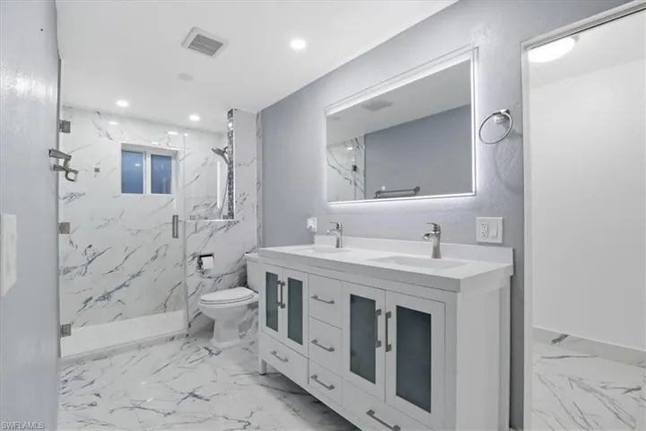 Bathroom with double vanity, a marble finish shower, and recessed lighting